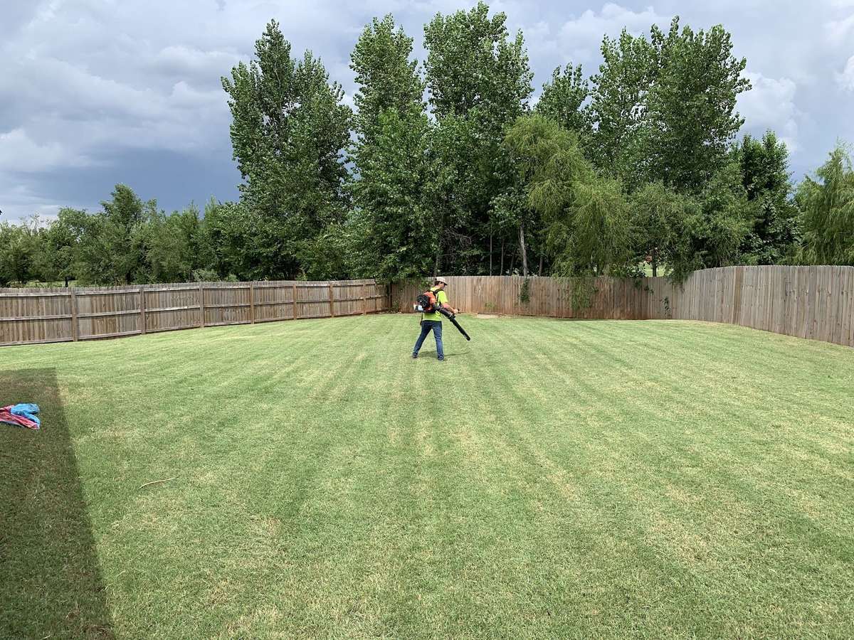 Spohn's Lawn worker using a backpack blower across a freshly mowed backyard.